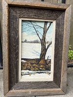 Original oil painting showing a vertical composition of a winter landscape with a bare tree and snow on the ground. The rustic reclaimed wooden frame is visible, emphasizing the natural texture.