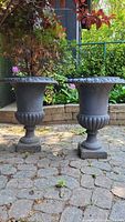 Two black ornate metal garden planters side by side on a patio