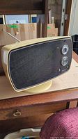 Side angle showing the TV's yellow casing, black front panel with tuning knobs, and speaker grille on sides.