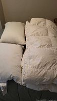 Photo showing queen size white quilted duvet with two pillows all laid out on bed surface.
