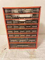 Front view of the red metal hardware storage organizer cabinet showing clear plastic drawers with assorted hardware inside.