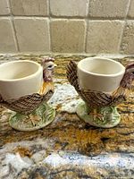 Two ceramic egg cups shaped as roosters with multicolored paint, shown on granite countertop