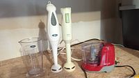 All three appliances shown together on countertop, includes measuring cup, two hand blenders, and mini food chopper.
