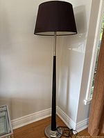 Full view of the tall floor lamp showing silver and dark brown metal-wood body and dark brown lampshade on a silver circular base.