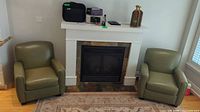 Two green leather accent chairs flanking a fireplace in a living room