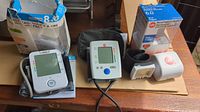 Three blood pressure monitors: Omron Bios Precision 8.0 with box, Life Brand BM35/1U, and Life Brand BC 30 with case and manuals