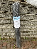 Photo of trafficMASTER black EVA foam floor mat rolled and sealed in original packaging against a brick wall.