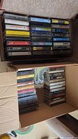 Box of assorted music cassette tapes, showing titles like Julio Iglesias, Gipsy Kings, and multiple others, stored in plastic cases.