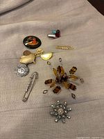 Photo showing all 9 unique vintage-style brooches and pins arranged on fabric, varying in color, metal, and beaded detail.