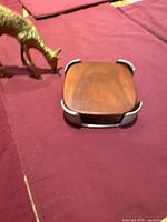 Photo showing brass grazing deer figurine and coaster caddy with a wood coaster on top on burgundy fabric.