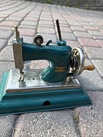 Side view showing teal enamel body, chrome needle area, and Casige eagle logo in gold.