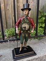 Front view of vintage gentleman clock figurine with floral clock and top hat, colorful painted metal on black base