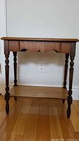 Front view of the vintage wooden side table showing decorative carved apron and turned legs, as well as lower shelf.