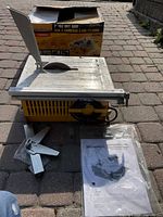 7 inch wet tile saw with blade guard, adjustable fence, manual and original box on paved ground.