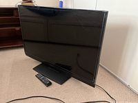 Front side view of the 34 inch Insignia TV with remote placed in front, showing screen and stand.
