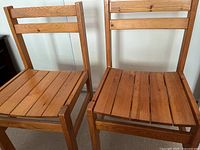 Two pine dining chairs side by side showing the front and side views with slatted wooden seat and backrest.