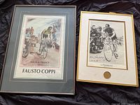 Two framed cycling prints placed side by side on a dark fabric background, showing a color illustration of Fausto Coppi and a black and white cycling photograph.