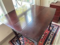 Photo of the folding table opened, showing the wooden top with some surface wear and scratches.