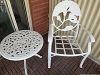 Full view of the wrought iron armchair and round table showing the intricate floral designs and overall structure of the furniture pieces.