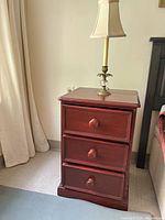 Wooden side table with three drawers, red-brown finish, standing on carpet.