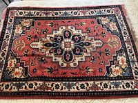Top view of a rectangular handmade wool carpet featuring a central medallion design in red, blue, beige, and other traditional colors.