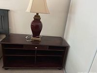 Solid wood TV stand with bookshelf compartments, dark finish, positioned against a wall with the lamp on top