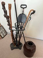 Photo of the metal cane stand holding various wooden canes and a foldable cane seat with a brown ceramic jar beside it.