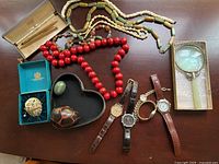 Overview photo showing entire lot of watches, necklaces, pen set, magnifying glass, and decorative boxes on table.