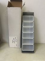 Bar top condiment caddy with six white removable containers and clear hinged lid, beside original packaging box.