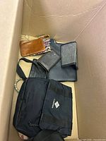 Top view of box with mixed wallets of various colors including brown, tan, and black along with a black Columbia pouch visible