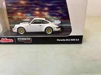 Side view close-up of white Porsche 911 RSR 3.8 model in display case with branded base and packaging visible.