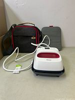 Cricut EasyPress 2 heat press machine connected to power cord, heat-resistant mat, and carrying case on a flat surface.