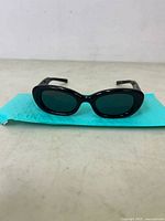 Front view of black framed sunglasses with dark lenses on a blue padded surface.