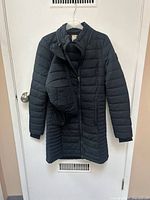 Full view of the black quilted jacket hanging on hanger showing front, zipper, sleeves, and length.