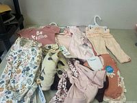 18 pieces of assorted new baby girl clothing, including bodysuits, pants, and tops in pastel and floral prints.