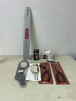 Image showing Oregon Pro-Steel chainsaw bar vertically positioned with other small tool and auto accessories including pliers and a glow plug ignitor on table.