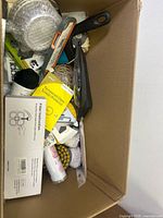 Top-down view of a cardboard box containing assorted items including brushes, sprays, screen protector and dustpan.