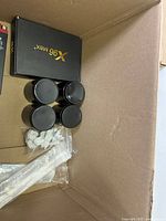 Box containing X96 Max device box, four black cylindrical objects, small white items, black level tool, and white plastic spoons.