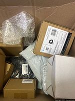 Box containing multiple smaller cardboard boxes, some bubble wrapped items, and plastic wrapped components, some visible cables.