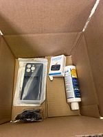 Box with black Koolife phone case, small white adapter, tube of adhesive or sealant, and some cables.