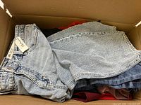 Overhead photo of a box showing folded denim jeans with Bootlegger tags, multiple garments stacked beneath