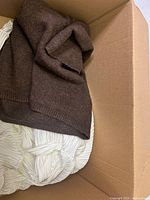 Clothing box with folded brown knit sweater and white striped fabric item underneath.