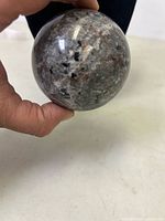 Photos showing a polished natural quartz sphere featuring Yooperlite mineral inclusions with mixed grey, black, and reddish highlights.