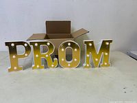 Four white illuminated marquee letters spelling PROM with LED bulbs, displayed with open box.