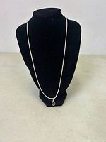 Full view of the necklace displayed on a black stand showing the silver chain and purple pendant.