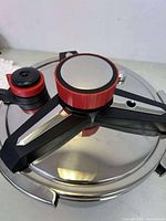 Close-up of pressure cooker lid with black and red handle and pressure valve.