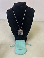 Full view of round pendant displayed on black bust with chain draped and Tiffany pouch beneath