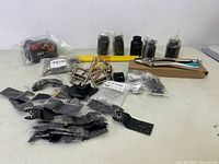 Assorted small black tools and accessories on a table including drill blades, clamps, and locking pliers.