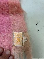 Close-up of the label showing "100% mohair", "Made in Scotland", and Hudson's Bay seal of quality stamp on a fuzzy pink and peach fabric.