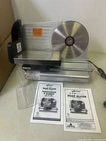 Weston electric meat slicer with stainless steel circular blade, sliding tray, two clear plastic food holders, and two manuals on a white surface.